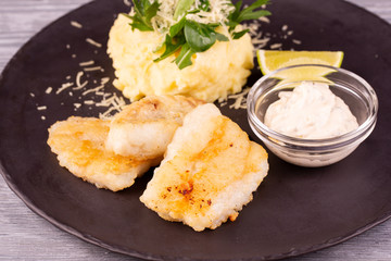 Cod fillet fried, served with mashed potatoes, grated cheese and cream sauce with chopped greens