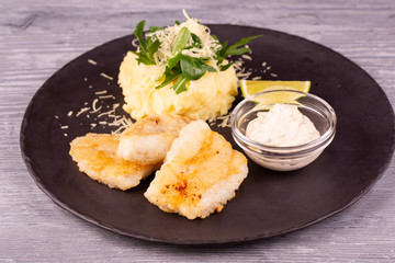 Cod fillet fried, served with mashed potatoes, grated cheese and cream sauce with chopped greens
