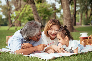Fototapeta premium Grandmother,Grandfather and grand daughter enjoying sunny garden holiday together, outdoors space, leisure lifestyle,happy teaching with flare light sky in park.