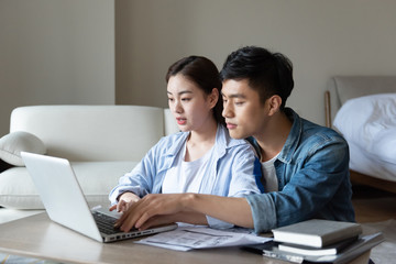 Obraz premium A young asian couple is sitting on a carpet using a computer