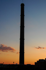 Fototapeta na wymiar old industrial chimney silhouetted against an orange sunset sky
