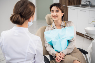 Smiling woman sitting in dentist's sitting and chatting to her doctor