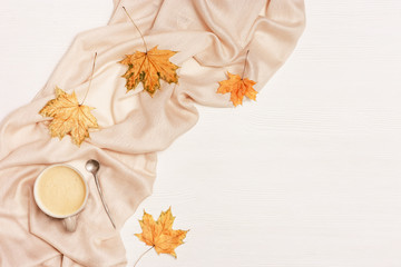 Autumn flat lay with cup coffee cappuccino and yellow autumnal leaves on white wooden background with copy space. Natural leaves of maple tree and cozy warm palantine. Top view.