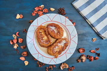Traditional homemade Spanish torrijas on blue wooden background  with flower ornament, milk with cinnamon and sugar and a cloth. Easter typical dessert.