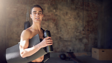 Fototapeta na wymiar Cheerful sportsman with rug and bottle on background of a blurred brick wall