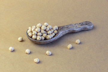 Dry chickpea in ceramic spoon on brown paper tablecloth.