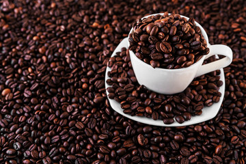 White mug and saucer next to roasted coffee beans everywhere, inside the mug and a lot around it. Great for going to a cafe, restaurant, cafeteria menu or as a sign