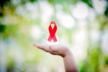 Aids red ribbon on hand bokeh nature background for world aids day and national hiv / aids concept...