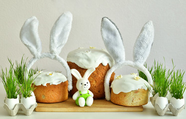 Easter orthodox sweet bread, multicolored eggs and bunny ears with green grass.Easter greeting card template. Easter sweets on light background.Holidays breakfast concept with copy space