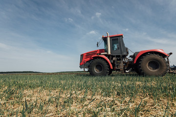 field and a red tractor moving along it during plowing in the summer
