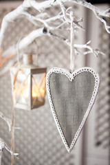 Biglietto grigio a forma di cuore appeso a dei rami dipinti di bianco , sullo sfondo una lanterna anch'essa appesa