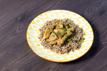 Stewed meat with boiled buckwheat  on plate on brown wooden background