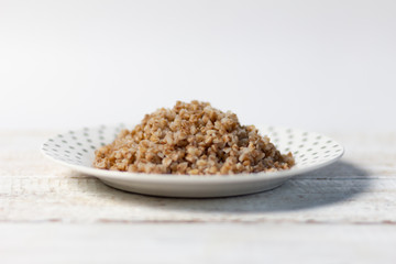 Boiled buckwheat on polka dot plate on white background