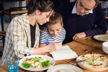 Young parents checking their daughter's homework. There are a few things to correct.