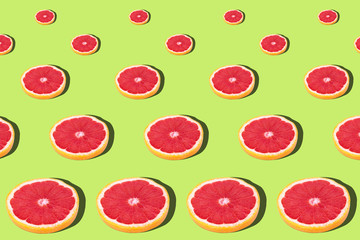 Flat lay fruit pattern of fresh grapefruit slices on green background.