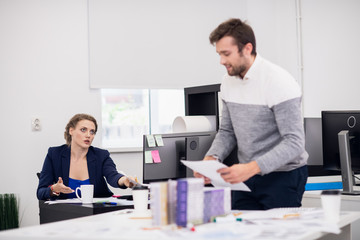 Young pretty woman handing out a blueprint to her male colleague in the office