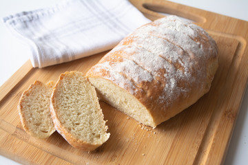 A loaf of homemade fresh bread with flour sprinkled on top in a kitchen towel on wooden cutting...