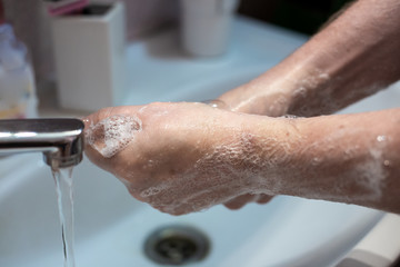 a man washes his hands with liquid soap over a sink at home