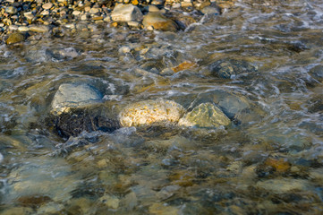 pebble stones on the sea beach, the rolling waves of the sea with foam