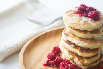 Fluffy pancakes with condensed milk and raspberries on a wooden plate with a kitchen napkin and a fork 
