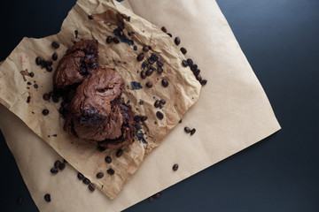 Homemade chocolate brownies and coffee beans on craft paper on dark black background. Brown gluten free carob cake. Copy space, top view, horizontal