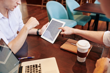 Marketing managers discussing charts with statistics on tablet computer when having meeting in coffeeshop