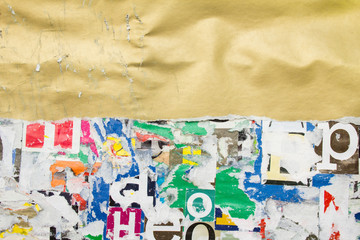 Torn, crumpled and scratched golden glossy paper placard on dirty billboard with old ripped and peeling pieces of paper posters background. Copy space for text.
