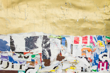 Torn, crumpled and scratched golden glossy paper placard on dirty billboard with old ripped and peeling pieces of paper posters background.