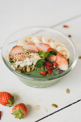 Smoothie bowl with banana and spirulina, almond flakes, chia seeds, pumpkin seeds and strawberry on white background.