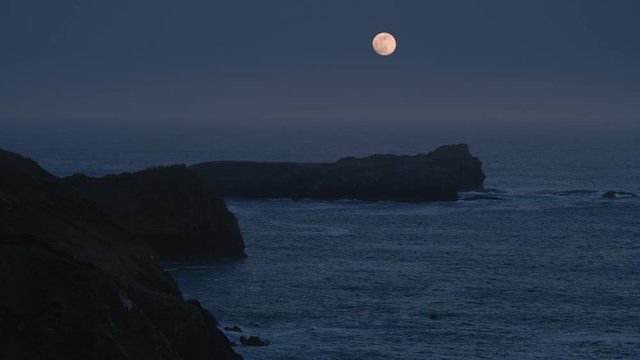 A super-moon over the ocean with cliffs in the foreground.