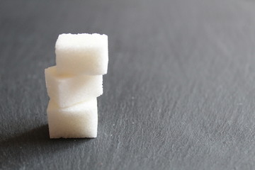 three or four lumps of sugar lie in a column on the table against a dark background