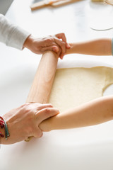Mother and son´s hands stretching pizza dough with a rolling pin