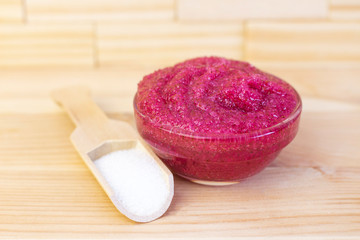 Natural pink body scrub made from sugar. Pink scrub in a glass cup on a background of candles and sugar.