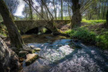Fototapeta na wymiar historic stone arch bridge crossing a little river, emotioanal landscape photography on a warm sunny spring 