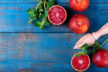 Blood oranges and wooden squeezer against the blue background. Top view. Copy space