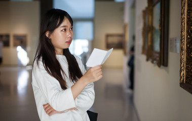 Chinese woman with guide-book near picture collection in the museum