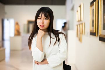 Serious chinese female visitor looking at artwork painting in museum