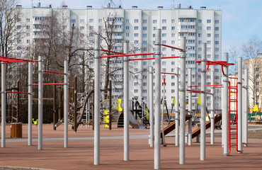 Fototapeta na wymiar Empty playground with swings and sports simulators for preschool and early school-age children in a residential area. Sunny day in early spring or late autumn. Horizontal orientation. Selective focus