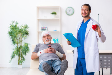 Fototapeta premium Young male doctor and old patient in first aid concept