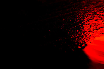 Abstract photo reflection of light on a wet surface. Red neon light on a textured wet surface. Reflection of light on the pavement. Glare on the water.