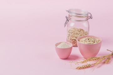 Bowl of dry oat flakes with oatmeal and ears of wheat on light background. Healthy skin, facial and body care.