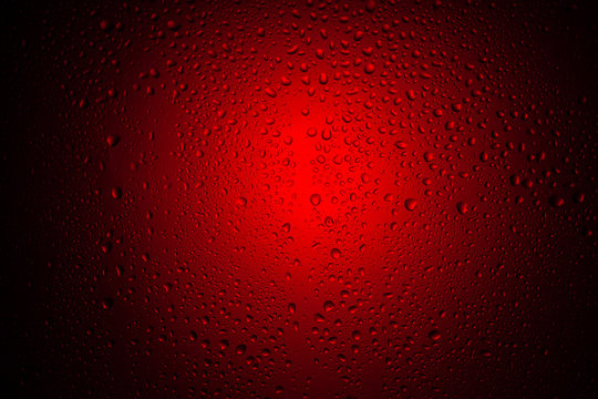 Drops of water on glass in red neon light. Rain on the glass against the background of colored lights. Abstract photo for background.