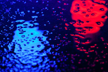 Abstract photo reflection of light on a wet surface. Blue and red neon light on a textured wet surface. Reflection of light on the pavement. Glare on the water.