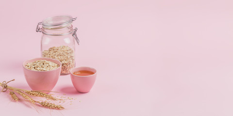 Bowl of dry oat flakes with honey and ears of wheat on light background