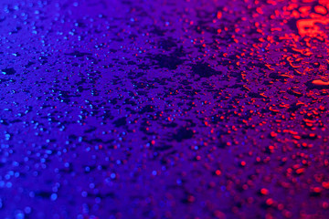 Drops of water on a textural surface in neon light. Reflection of red-blue light in drops of water. Dark photo.