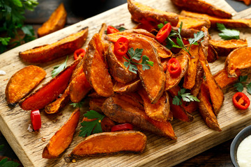 Healthy Baked Orange Sweet Potato wedges with dip sauce, herbs, salt and pepper on wooden board