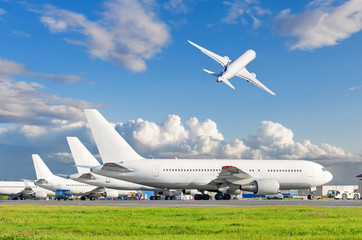 View of the standing planes at the airport and airplane taking off in the sky.
