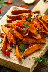Healthy Baked Orange Sweet Potato wedges with dip sauce, herbs, salt and pepper on wooden board