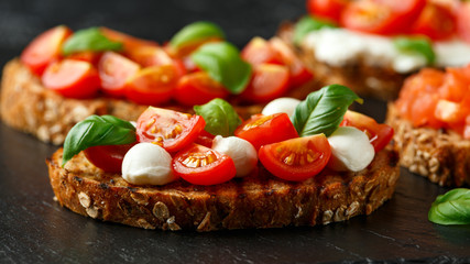 Bruschetta with mozzarella cheese, basil, cherry tomato on rustic stone board