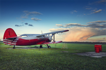 Fototapeta na wymiar Old red biplane on a green field at sunset